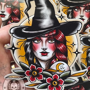 May include: A die-cut sticker featuring a stylised illustration of a person wearing a black pointed witch hat. The figure has dark hair with red highlights, red cheeks, and red lips. The design includes two red flowers, a yellow crescent moon, and stars.