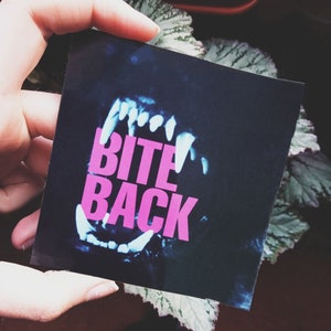May include: A black and blue image of a mouth with teeth, with the words "BITE BACK" in pink letters.