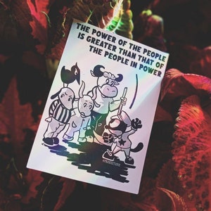 Può includere: Un adesivo con un'illustrazione in bianco e nero di quattro animali dei cartoni animati. Gli animali sono un cane, una mucca, una pecora e un gatto. L'adesivo ha una finitura olografica e il testo "THE POWER OF THE PEOPLE IS GREATER THAN THAT OF THE PEOPLE IN POWER" è stampato su di esso.