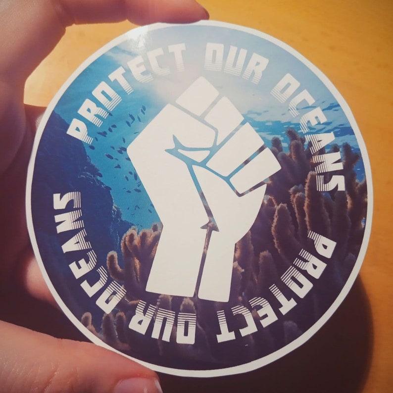 May include: A white fist raised in the air with the text "Protect Our Oceans" repeated twice around the fist. The background is a blue ocean with coral reefs.