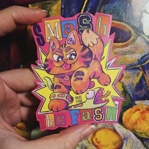 Pode incluir: Um adesivo colorido com um gato de desenho animado com uma estrela amarela no peito, montando uma cobra com as palavras "Smash the Fash" em uma fonte arco-íris.