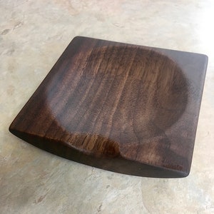 May include: A dark brown wooden bowl with a rounded, slightly curved bottom. The bowl is made of a dark wood with a smooth finish.