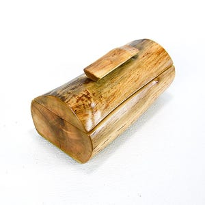 May include: A wooden box with a natural wood finish. The box is shaped like a log and has a hinged lid. The lid is held closed by a small wooden latch.