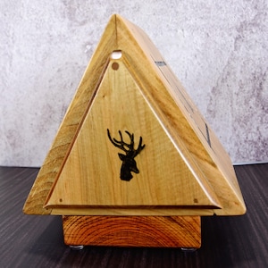 Puede incluir: Una caja de madera triangular con un diseño de silueta de ciervo en la parte delantera. La caja tiene un acabado de madera natural y una base marrón oscuro.