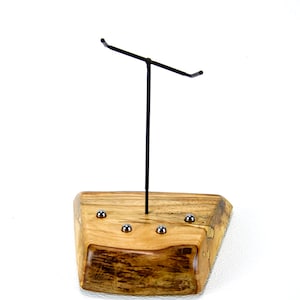 May include: A wooden jewellery display stand with a black metal T-shaped arm. The base is a rectangular block of light brown wood with a natural edge and embedded silver-coloured spheres. The stand is designed to hold necklaces or other jewellery.