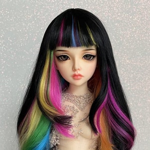 Puede incluir: Una peluca negra para muñeca con cabello largo y ondulado. La peluca tiene mechones amarillos, verdes, azules, rosas y naranjas.