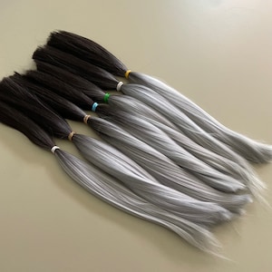 Puede incluir: Un conjunto de ocho extensiones de cabello con un color degradado de marrón oscuro a gris claro. Las extensiones están atadas juntas con gomas elásticas de colores.