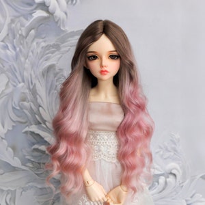 Könnte beinhalten: Eine Puppe mit langen, welligen, ombre-Haaren. Die Haare sind an den Wurzeln braun und verblassen zu den Spitzen hin zu rosa. Die Puppe trägt ein weißes Kleid mit Spitzenbesatz.