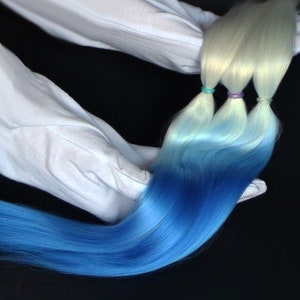 Puede incluir: Tres mechones de extensiones de cabello ombré, que pasan de blanco a azul claro a azul oscuro. El cabello se mantiene en su lugar con gomas elásticas de colores.