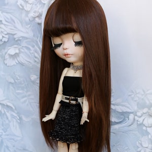 Puede incluir: Una muñeca con el pelo largo y castaño que lleva un vestido negro sin tirantes con un cinturón dorado y una falda con estampado blanco y negro.