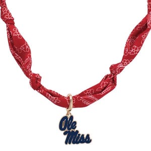 May include: A red bandana necklace with a white paisley pattern. The necklace features a gold-colored charm with the words "Ole Miss" in blue and white enamel.