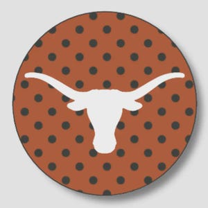 May include: A circular sticker featuring a burnt orange background with a repeating pattern of small dark gray polka dots. Centered on the sticker is a solid white silhouette of a longhorn steer head with prominent, wide-reaching curved horns.
