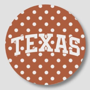 May include: A circular sticker featuring a burnt orange background with a repeating pattern of small white polka dots. Centered on the sticker is the word TEXAS written in large, bold, white block capital letters with a slight arching curve.