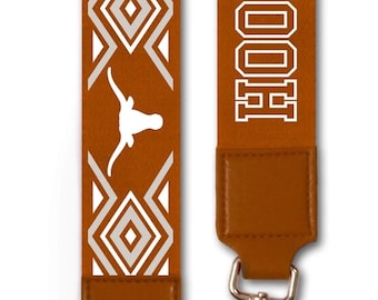 May include: Two brown and white patterned straps with silver hardware. One strap features the text "HOOK 'EM, HORN" in white. The other strap has a geometric design with a longhorn silhouette. The straps have brown leather ends.