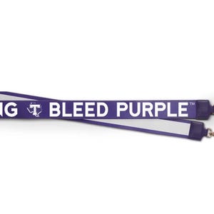 May include: Purple lanyard with white text that reads "BLEED PURPLE" and a small white logo of a "T" with a star inside. The lanyard has two gold clasps.