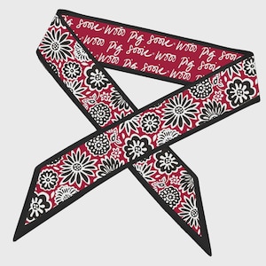 May include: A decorative scarf with a floral pattern in black and white on a burgundy background. The scarf has a black border and the words "Soove Wood Pig" are repeated in white.