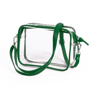 May include: A rectangular clear crossbody bag featuring vibrant green trim and a matching green adjustable shoulder strap. The bag includes a top zipper closure with a green pull tab and silver-toned metal hardware clips on each side.
