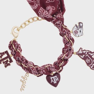 May include: Maroon and gold bracelet featuring a paisley pattern. The bracelet includes gold chain links and charms with the letters "A&M", a heart, a football helmet, and a howling wolf. The word "Aggies" is also included.