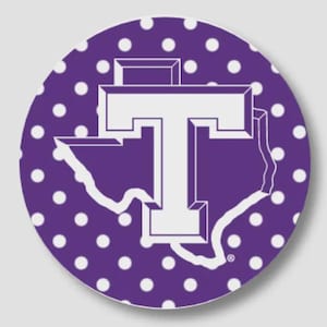May include: A circular sticker featuring a purple background with a white polka dot pattern. Centered on the sticker is a white outline of the state of Texas with a large, bold white letter T superimposed over the center of the state shape.