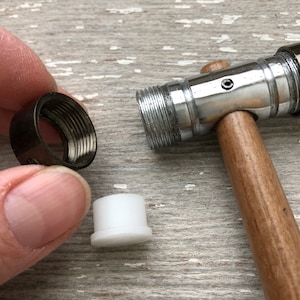 May include: A close-up of a wooden mallet with a silver metal head. The mallet is lying on a wooden surface. There are two small metal and plastic objects next to the mallet.