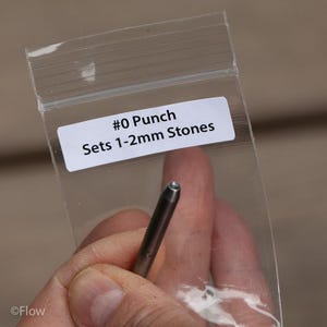 May include: A #0 metal punch tool designed for setting 1-2mm stones, enclosed in a clear plastic bag with a white label that reads #0 Punch Sets 1-2mm Stones. The tool is cylindrical with a tapered tip and a small circular opening at the end.