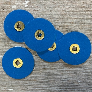 May include: Five blue sanding discs with gold-coloured centres. The discs are arranged in a semi-circle on a wooden surface.