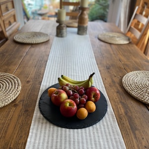 Peut inclure: Un plateau de service en ardoise noire avec une variété de fruits, dont des pommes, des raisins et des abricots. Le plateau est posé sur un chemin de table rayé blanc et gris.