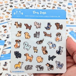 Puede incluir: Una hoja de pegatinas de vinilo resistentes al agua con varios perros de dibujos animados. Las pegatinas son de varios colores y tienen el texto "Tiny Dogs" sobre un fondo azul.