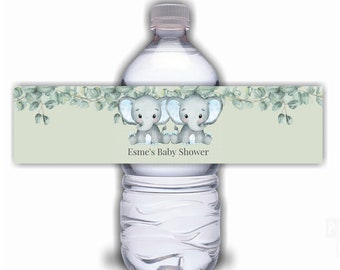 May include: Water bottle label with two gray baby elephants with blue ears, green eucalyptus leaves, and the text "Esmé's Baby Shower".