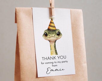 May include: A white thank you tag with a green snake wearing a yellow and orange party hat. The text on the tag reads "Thank you for coming to my party from Emmie".