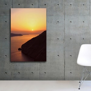 May include: A photograph of a sunset over a body of water with a rocky cliff in the foreground. The sky is a vibrant orange and yellow, and the sun is setting in the distance. The water is a deep blue, and the cliff is a dark brown.
