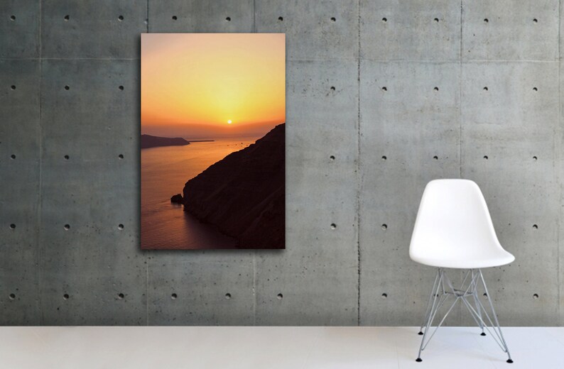May include: A photograph of a sunset over a body of water with a rocky cliff in the foreground. The sky is a vibrant orange and yellow, and the sun is setting in the distance. The water is a deep blue, and the cliff is a dark brown.