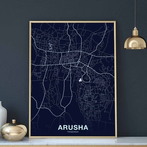 May include: A navy blue map print of Arusha, Tanzania, with white lines showing the city streets. The map is framed in a gold frame and is hanging on a dark gray wall.