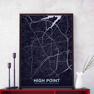 Può includere: Una stampa di mappa in bianco e nero di High Point, Carolina del Nord, Stati Uniti. La mappa è incorniciata in una cornice nera ed è esposta su uno scaffale con due portacandele neri e un vaso bianco con steli verdi.