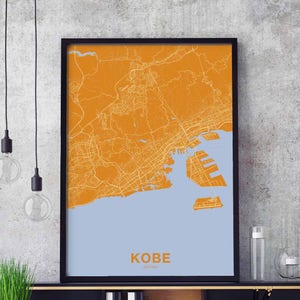Puede incluir: Un mapa enmarcado de Kobe, Japón, con un fondo azul claro y líneas naranjas que representan las calles y vías fluviales de la ciudad. El nombre de la ciudad "KOBE" y "JAPÓN" están impresos en negro en la parte inferior del mapa.