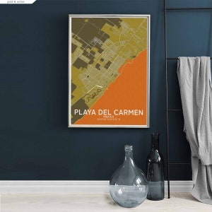 Puede incluir: Un mapa enmarcado de Playa del Carmen, M&eacute;xico, con un esquema de color dorado y ocre. El mapa est&aacute; colgado en una pared azul oscuro, con un jarr&oacute;n de vidrio transparente y una botella de vidrio oscuro en un suelo blanco en primer plano.