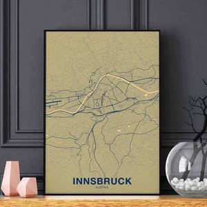 May include: A beige and blue map print of Innsbruck, Austria, with the city name and country printed at the bottom of the map. The map is framed in a black frame and is hanging on a gray wall.