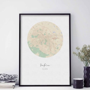 Puede incluir: Una impresión enmarcada en negro de un mapa de Sofía, Bulgaria. El mapa está en un círculo y está en tonos beige, verde y marrón. El nombre de la ciudad "Sofía" y el nombre del país "Bulgaria" están escritos en negro debajo del mapa.