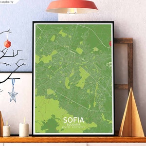 Puede incluir: Una impresión de mapa verde y blanco de Sofía, Bulgaria. El mapa está enmarcado en un marco negro y está colgado en una pared. El mapa está rodeado por una pared blanca, un estante de madera y una escalera de madera.