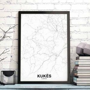 May include: A black framed print of a map of Kukës, Albania. The map is in a white and grey colour scheme and shows the roads and rivers of the area. The print is hanging on a white brick wall.