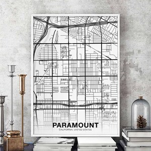 Puede incluir: Una impresión enmarcada en blanco y negro del mapa de Paramount, California, Estados Unidos. La impresión se exhibe sobre una mesa con candelabros decorativos y libros. El mapa presenta una superposición de cuadrícula.