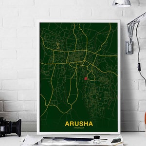 May include: A green and gold map print of Arusha, Tanzania. The map shows the city's streets and roads in gold, with a red dot marking the city center. The print is framed in white.