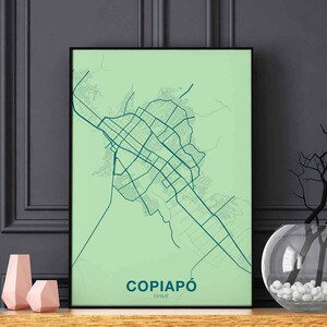 Può includere: Una stampa di mappa verde e blu di Copiapó, Cile, in una cornice nera. La mappa mostra le strade e le strade della città. La stampa è appesa a un muro grigio.