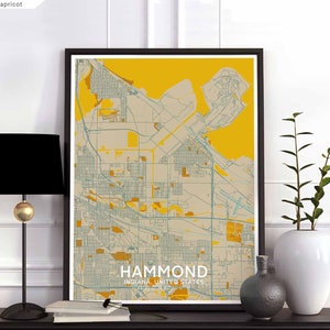 May include: A framed map of Hammond, Indiana, United States, with a yellow background and blue and white lines representing streets and roads. The map is displayed on a white wall with a black lamp and a vase with a plant on a black table.