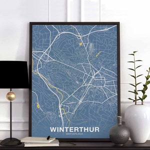 May include: A blue and white map print of Winterthur, Switzerland, in a black frame. The map is a detailed street map of the city. The print is hanging on a white wall.