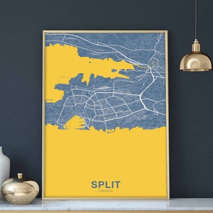 Puede incluir: Un mapa enmarcado de Split, Croacia, con un fondo amarillo y líneas azules que representan calles y vías fluviales. El nombre de la ciudad "SPLIT" y "CROATIA" están impresos en azul en la parte inferior del mapa.