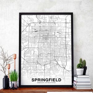 Pode incluir: Impressão de mapa em preto e branco de Springfield, Missouri, Estados Unidos, em uma moldura preta. O mapa mostra as ruas e os bairros da cidade. A impressão está pendurada em uma parede branca com uma prateleira de madeira abaixo.