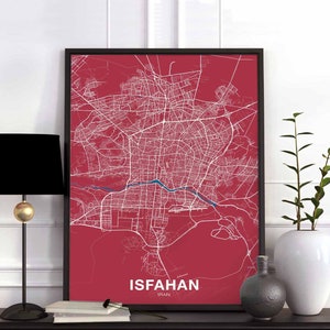 May include: A red and white city map print with the text "ISFAHAN, IRAN" at the bottom. The map is framed in a black frame and is displayed on a shelf with a black lamp and a vase.