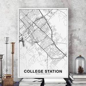 May include: Black and white map print of College Station, Texas, United States. The map shows the city's streets and landmarks. The print is framed in a white frame and is hanging on a wall.