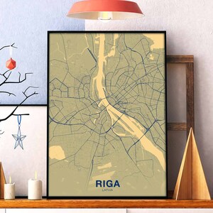 Peut inclure: Une carte encadrée de Riga, en Lettonie, avec un fond beige et des lignes bleues représentant les rues. La carte est encadrée en noir et porte l'inscription "RIGA" et "LATVIE" en bleu en bas.